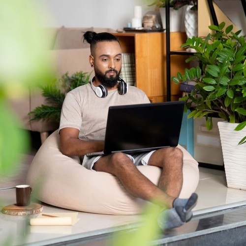 Picture of young man casually using a laptop in his home sitting on a beanbag chair